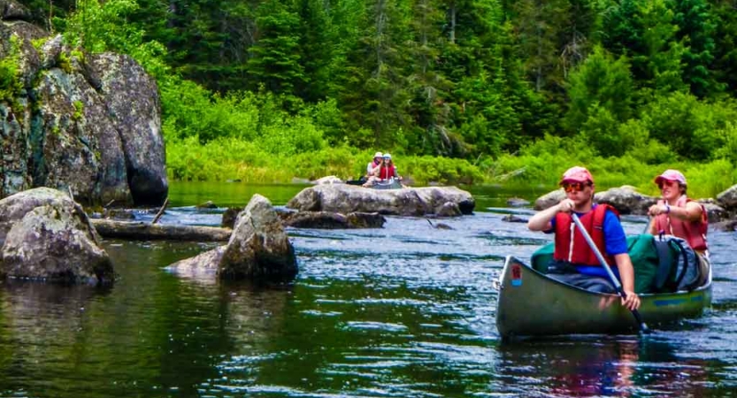 two students paddle a canoe between rocks with another canoe in the background